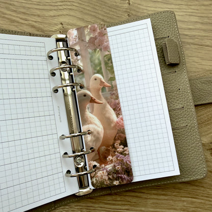 Open planner with grid pages and a decorative insert featuring ducks on a wooden surface